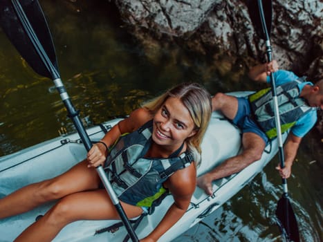 A young couple enjoying an idyllic kayak ride in the middle of a beautiful river surrounded by forest greenery.