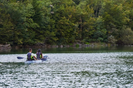 A young couple enjoying an idyllic kayak ride in the middle of a beautiful river surrounded by forest greenery.