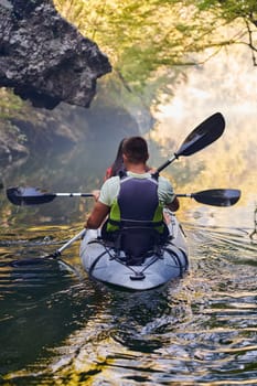 A young couple enjoying an idyllic kayak ride in the middle of a beautiful river surrounded by forest greenery.