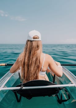 Woman in kayak back view. Happy young woman with long hair floating in transparent kayak on the crystal clear sea. Summer holiday vacation and cheerful female people having fun on the boat.