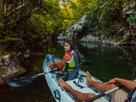 A young couple enjoying an idyllic kayak ride in the middle of a beautiful river surrounded by forest greenery.