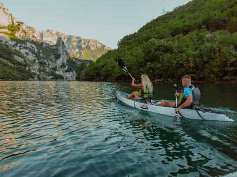 A young couple enjoying an idyllic kayak ride in the middle of a beautiful river surrounded by forest greenery.