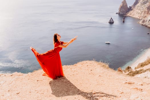 Woman red dress sea. Female dancer posing on a rocky outcrop high above the sea. Girl on the nature on blue sky background. Fashion photo