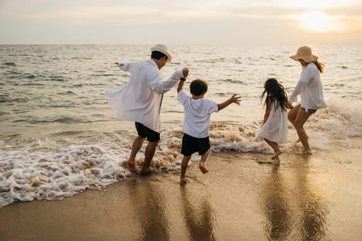 A joyful Asian family back view enjoys quality time on beach. Parents and daughters bond playing and pretending to fly with arms outstretched. carefree and happy weekend moment captured under sun.