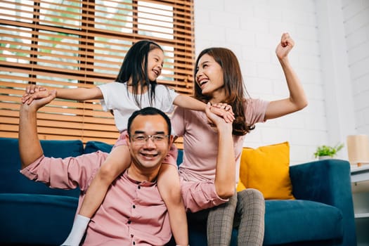 A happy Asian family father mother and daughter enjoy quality time on a comfortable sofa in their modern house experiencing togetherness and joy during self-isolation.