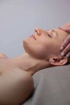 Caucasian woman undergoing a head and face massage procedure. Vertical photo