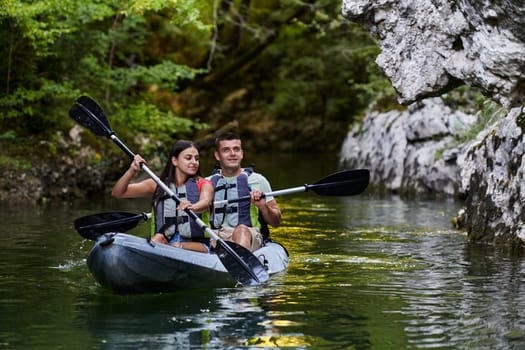 A young couple enjoying an idyllic kayak ride in the middle of a beautiful river surrounded by forest greenery.