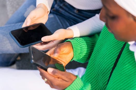 close up of the hands of two unrecognizable women using their mobile phones, concept of technology of communication and modern lifestyle