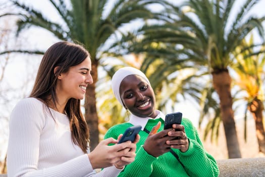 two young female friends smiling happy using mobile phone sitting in a city park, concept of technology of communication and urban lifestyle, copy space for text