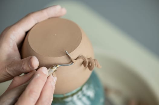 A potter works with a tool on a potter's wheel. Close-up of a man's hands