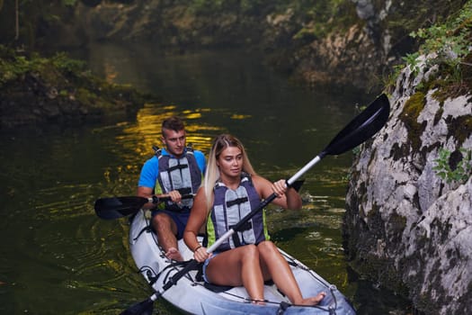 A young couple enjoying an idyllic kayak ride in the middle of a beautiful river surrounded by forest greenery.