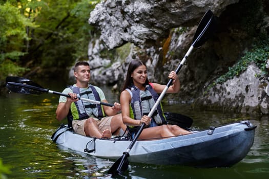 A young couple enjoying an idyllic kayak ride in the middle of a beautiful river surrounded by forest greenery.