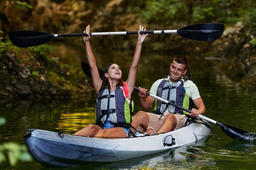 A young couple enjoying an idyllic kayak ride in the middle of a beautiful river surrounded by forest greenery.