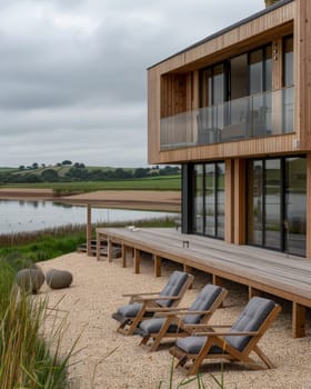 A modern, wooden cabin-style home sits on the edge of a tranquil lake, offering a peaceful outdoor deck area with comfortable lounge chairs overlooking the scenic landscape