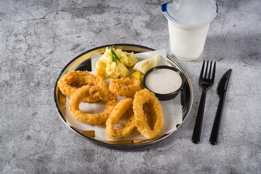 Fried calamari with potato salad next to it on stone table