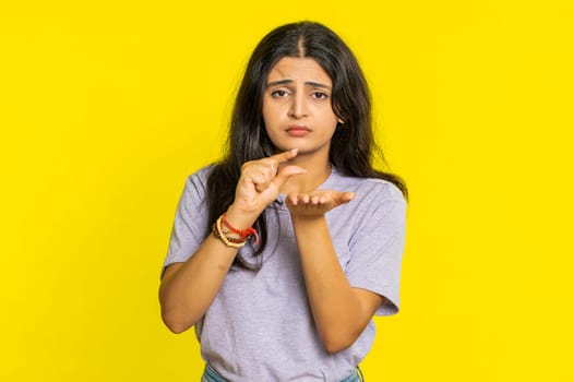 Need some more, please give me. Indian woman showing a little bit gesture with sceptic smile showing minimum sign, measuring small size, begging help. Arabian girl isolated on yellow studio background