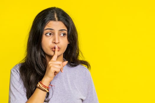 Shh be quiet please. Indian young woman presses index finger to lips makes silence gesture sign do not tells secret, stop talk gossip, confidential privacy. Arabian girl isolated on yellow background