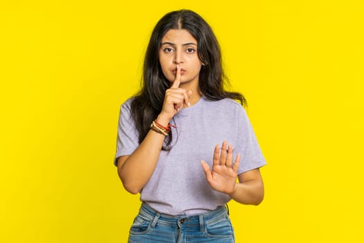 Shh be quiet please. Indian young woman presses index finger to lips makes silence gesture sign do not tells secret, stop talk gossip, confidential privacy. Arabian girl isolated on yellow background