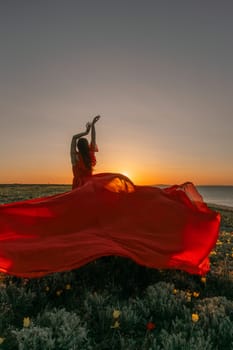 A woman in a red dress is standing in a field with the sun setting behind her. She is reaching up with her arms outstretched, as if she is trying to catch the sun. The scene is serene and peaceful