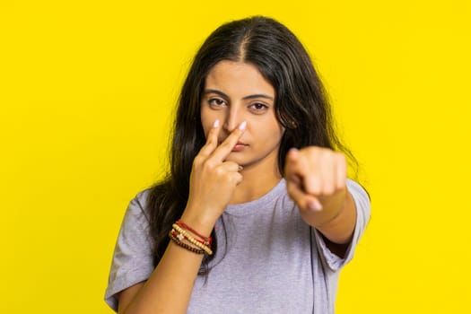 I am watching you. Confident attentive woman pointing at her eyes and camera, show I am watching you gesture spying on someone. Pretty disappointed Indian girl isolated on yellow studio background
