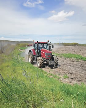 A robust red tractor plows through a field, kicking up dust and preparing the soil for planting. The powerful machine navigates the uneven terrain with ease, showcasing its agricultural prowess