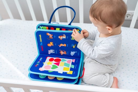 Little baby girl playing with busy book while sitting in crib. Concept of smart quiet books and modern educational toys