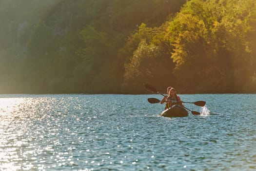 A young couple enjoying an idyllic kayak ride in the middle of a beautiful river surrounded by forest greenery in sunset time.