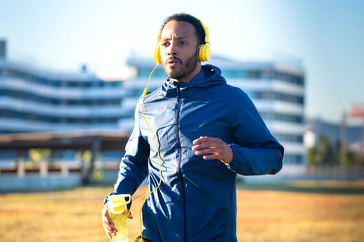 Young latino athlete with headphones training outdoors.