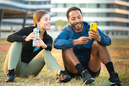Photo of a young couple using a social media app on smartphone while exercising outdoors.