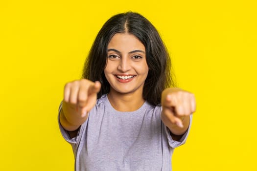 I choose you. Indian smiling woman pointing finger to camera and looking with playful happy expression, making winner choice, showing direction. Arabian young girl isolated on yellow studio background