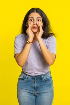 Keep my secrets, silence. Indian woman whisper news rumors holding hands near mouth share gossip quiet. Arabian girl telling interesting confidential story isolated on yellow background. Vertical