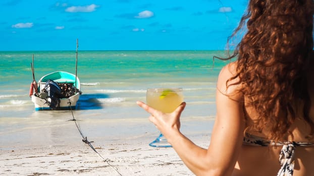 Woman holding a fruit cocktail on a white sand beach in summer. High quality photo