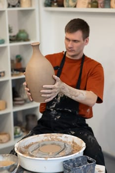 A man makes a ceramic vase on a pottery wheel. Vertical photo