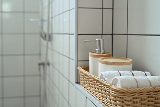 Wicker basket with white cotton towels and shampoo bottles inside a bright bathroom.