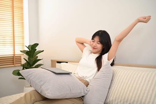 Positive young woman stretching body with satisfied face expression on couch at home.