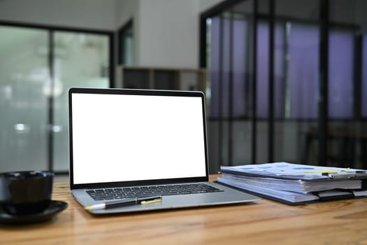 Laptop computer with white screen, cup of coffee and financial reports on wooden table.