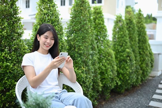 Portrait of charming young woman enjoy relaxing in the garden and using mobile phone.