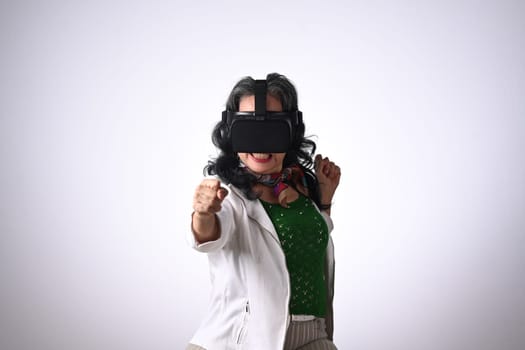 Joyful senior woman in boxing stance, playing action simulator game in VR headset.