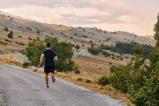 A muscular male athlete runs along a rugged mountain path at sunrise, surrounded by breathtaking rocky landscapes and natural beauty.