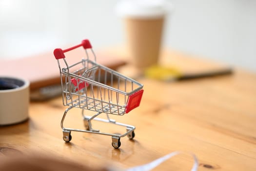 Empty shopping cart on wooden table at tailors studio. E-commerce, online shopping and small business concept.