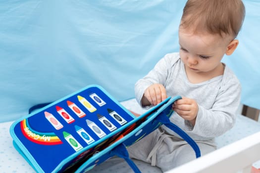 One year old baby playing with montessori busy book sitting in crib