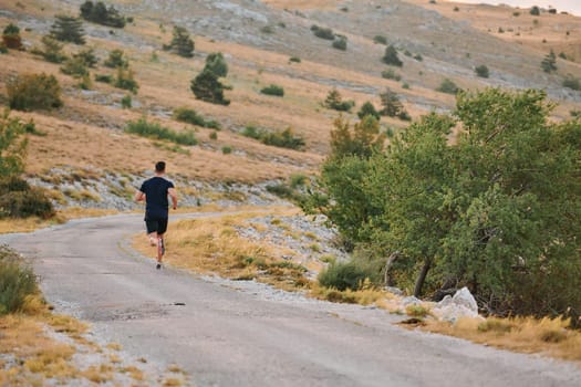 A muscular male athlete runs along a rugged mountain path at sunrise, surrounded by breathtaking rocky landscapes and natural beauty.