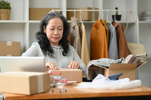 Mature woman small business owner preparing products for deliver to customers. E-commerce concept.