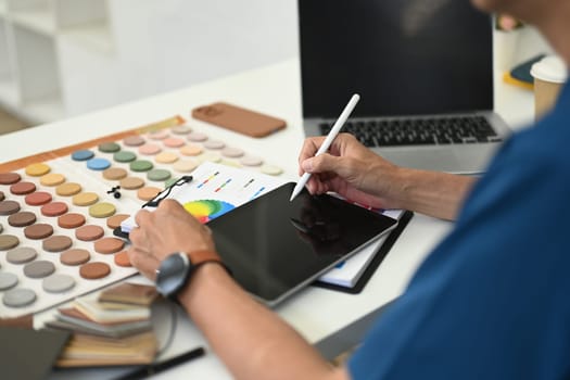 Cropped shot male interior designer using digital tablet at working desk with color swatch samples.