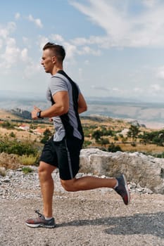 A muscular male athlete runs along a rugged mountain path at sunrise, surrounded by breathtaking rocky landscapes and natural beauty.