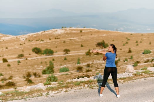 A determined female athlete stretches her muscles after a strenuous run through rugged mountain terrain, surrounded by breathtaking rocky landscapes.