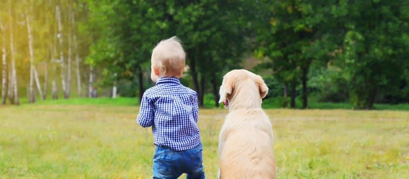 Child and Golden Retriever dog obedient sitting together in summer park, back view