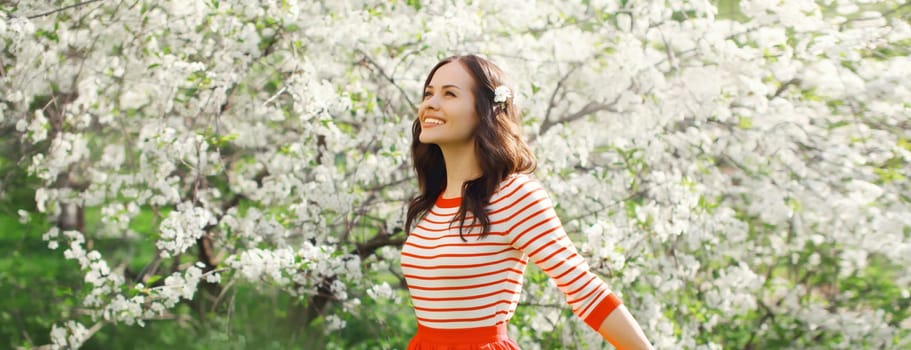 Lovely happy smiling young woman enjoying sunny day in spring blooming garden with white flowers on the trees in park