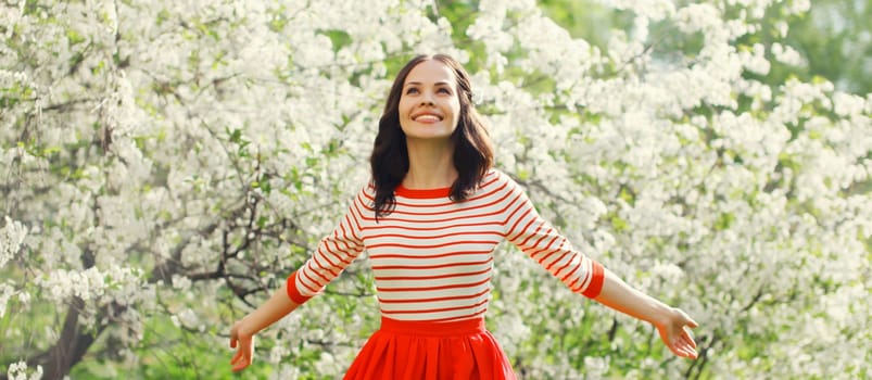 Lovely happy smiling young woman enjoying sunny day in spring blooming garden with white flowers on the trees in park
