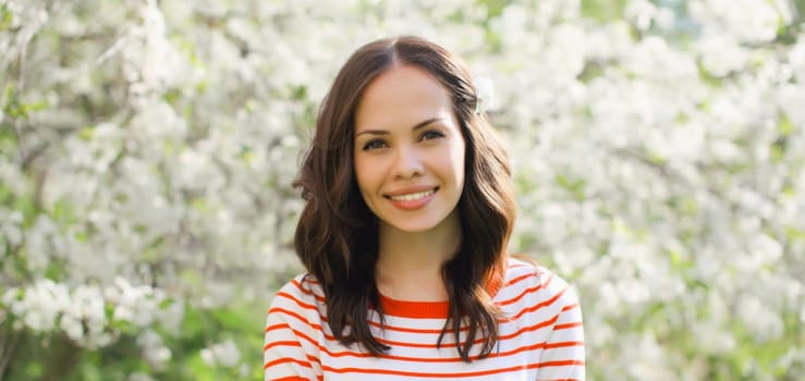 Portrait of lovely happy smiling young woman in spring blooming garden with white flowers on the trees in park